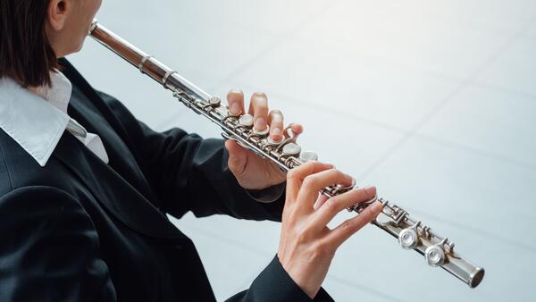 Bild vergr&ouml;&szlig;ern: Man sieht den Ausschnitt einer Frau von schräg hinten, sie hält eine Querflöte in beiden Händen.