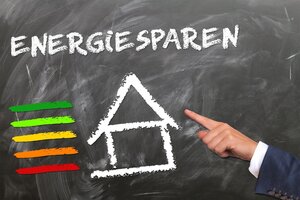 Ein ausgestreckter Finger zeigt auf eine Tafel, auf welcher ein Haus mit der Überschrift Energiesparen geschrieben ist.