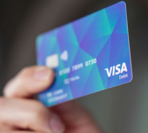 Hand die eine blaue Visa Kreditkarte hält.